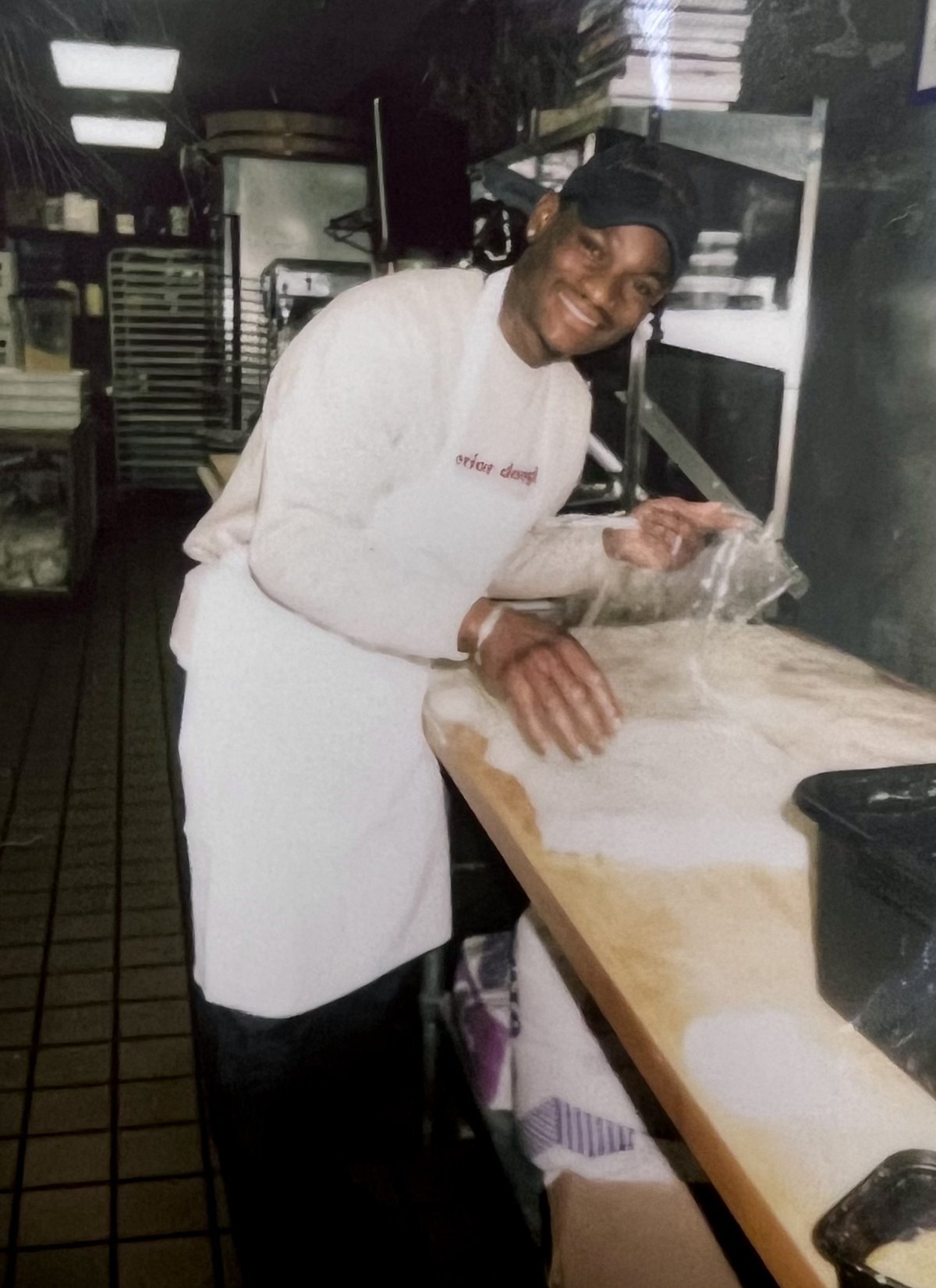 The founder in a bakery kitchen, smiling, one hand in the flour on the bench